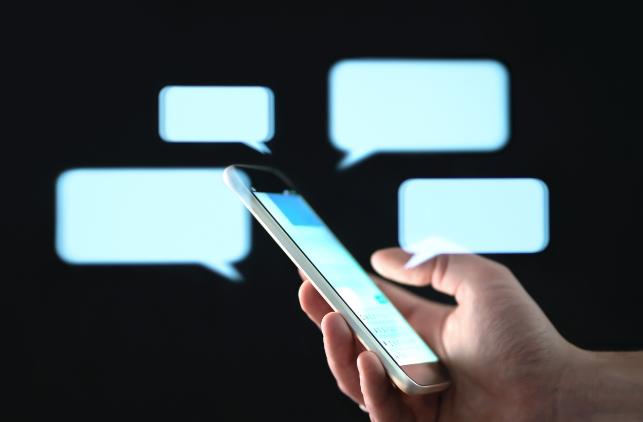 Text messages in cellphone screen with abstract hologram speech bubbles. Instant messaging app. Texting, group chat, sexting or sms concept.